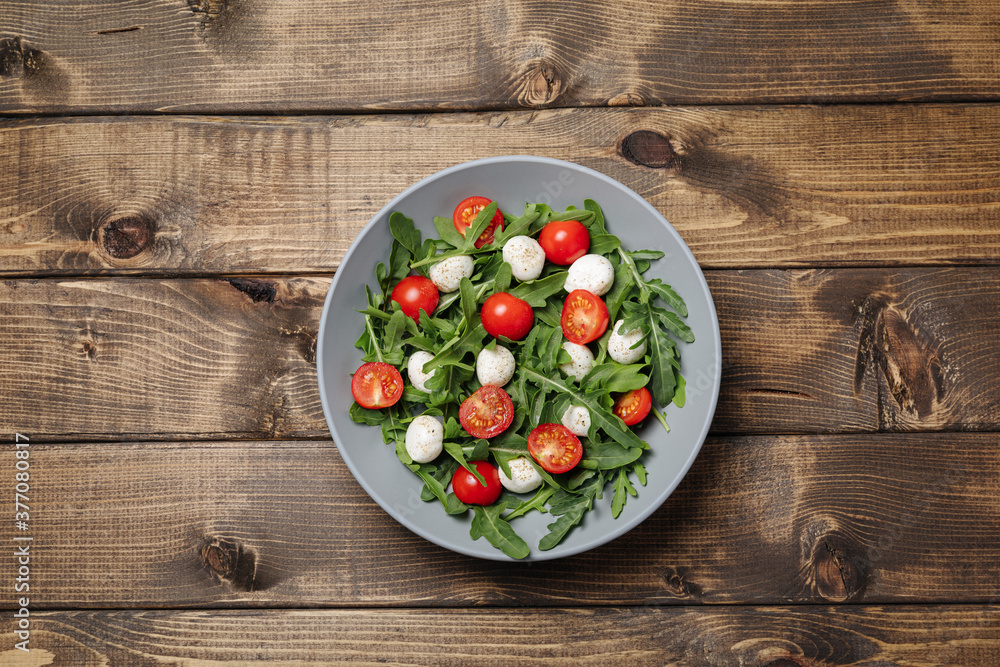 Diet and healthy salad with arugula, cherry tomatoes, mozzarella cheese on wooden background Diet and healthy salad with arugula, cherry tomatoes, mozzarella cheese on wooden background