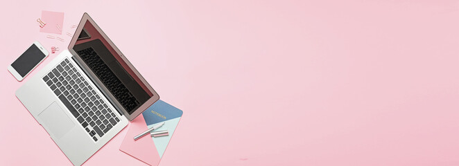 Laptop with office supplies and mobile phone on pink background