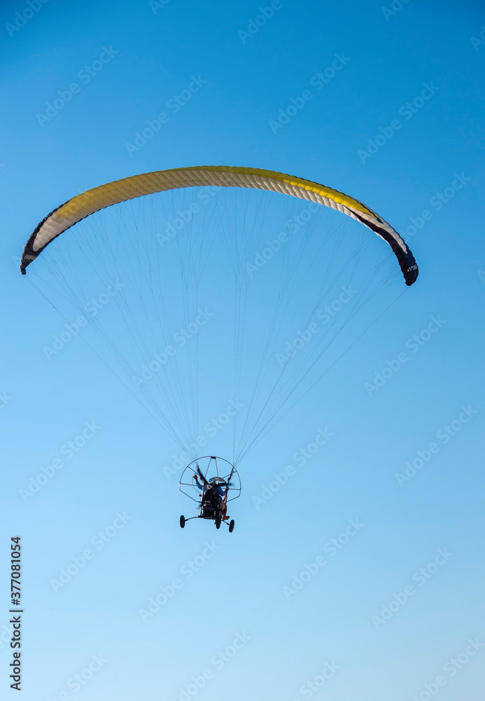 A paraglider with a yellow parachute against a clear blue sky. A paraglider with a yellow parachute against a clear blue sky.
