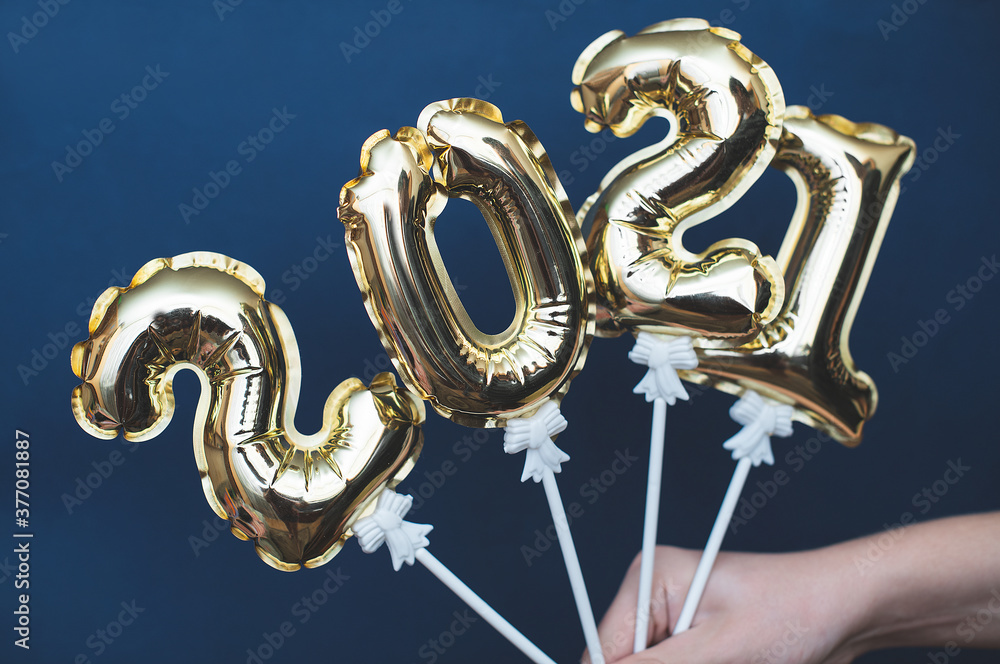 Hands up holding the Golden numbers 2021 from new year's balls of yellow metallic color on a blue background. Hands up holding the Golden numbers 2021 from new year's balls of yellow metallic color on a blue background.