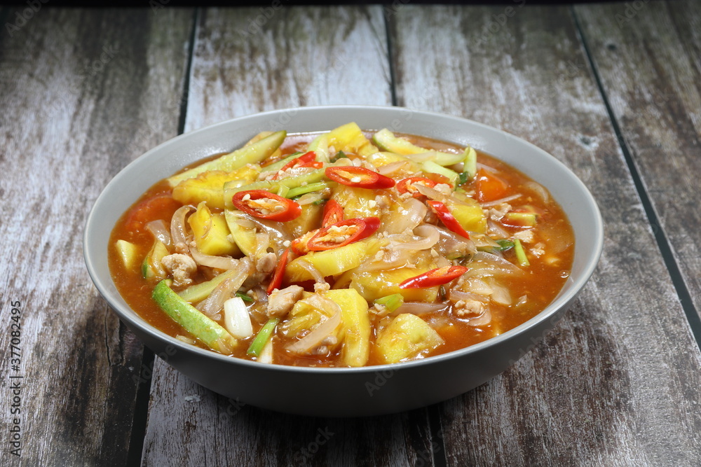 Traditional fried and stirred chopped fresh tomato, pineapple, cucumber and sliced onion in the bowl. Famous ancient red soup of vegetable in Chinese restaurant. Sweet and sour soup concept. 