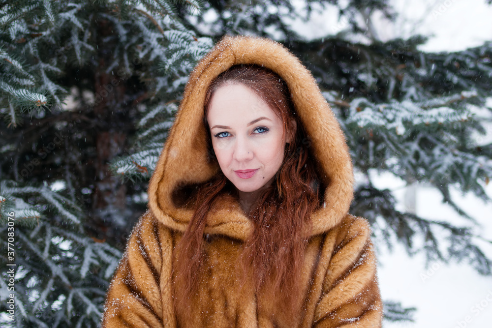 Portrait of young beautiful woman with red hair and blue eyes in faux fur coat on background of winter snowy park. Portrait of young beautiful woman with red hair and blue eyes in faux fur coat on background of winter snowy park.
