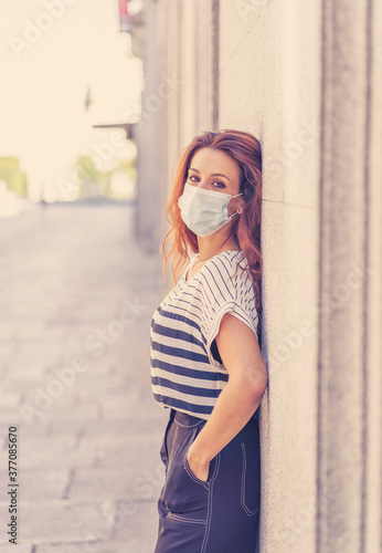 Portrait of red haired young happy woman wearing protective surgical face mask in public space