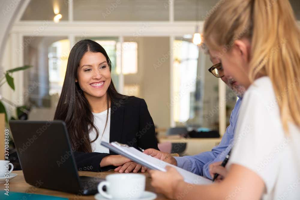 Couple of customers meeting with agent and reading insurance agreement. Young woman in formal jacket smiling and looking at clients. Business meeting concept Couple of customers meeting with agent and reading insurance agreement. Young woman in formal jacket smiling and looking at clients. Business meeting concept
