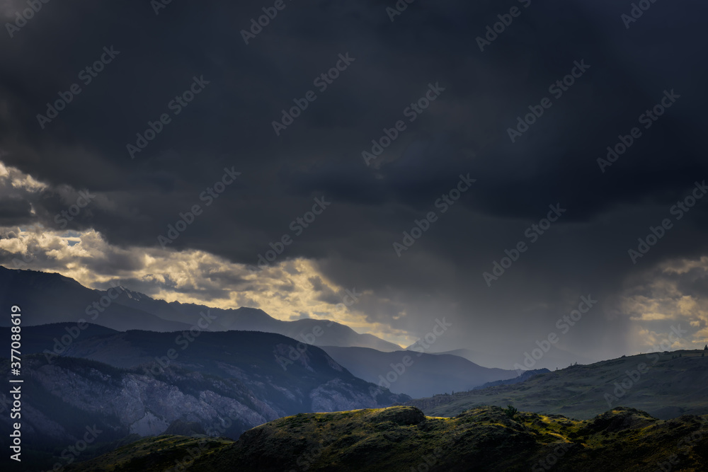Dramatic dark clouds in mountains before storm. Landscape with mountain range, rain clouds and rays from the sun. Epic natural background.