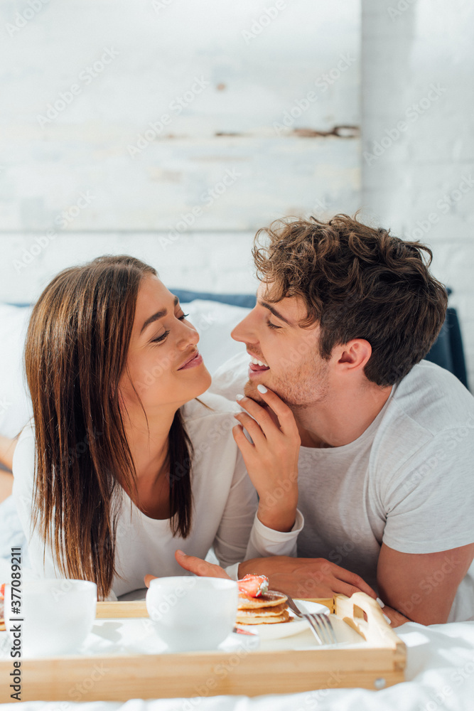 Selective focus of woman touching boyfriend near breakfast and coffee on bed Selective focus of woman touching boyfriend near breakfast and coffee on bed