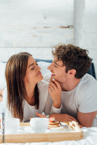 Selective focus of woman touching boyfriend near breakfast and coffee on bed