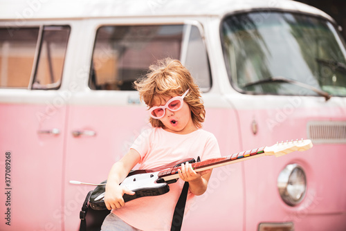 Child musician playing the guitar like a rockstar on pink background in neon light. Caucasian little boy learning to play guitar. photo