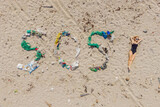 SOS inscription and woman sunbathes on the beach nearby. Environmental problem. Ecology concept. Plastic on the beach with sos writing. Spilled garbage on the beach