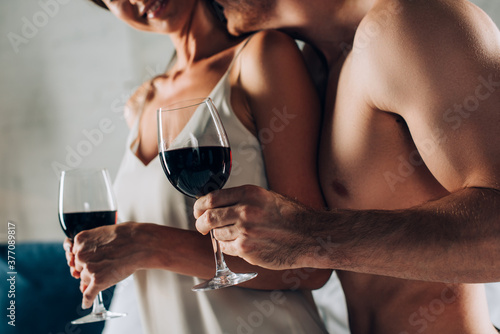 Cropped view of muscular man holding glass of wine and kissing seductive woman at home © LIGHTFIELD STUDIOS