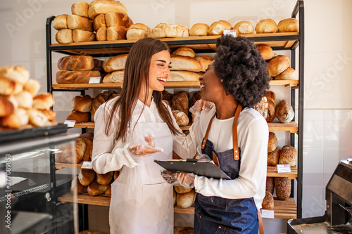 Shot of a young woman showing her colleague something on her clipboard while they stand in their bakery shop. Couple partnership the bakehouse with busness photo