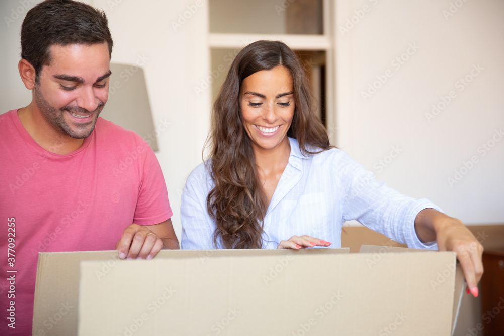 Joyful young Latin man and woman moving and unpacking things, opening carton box and looking inside. Relocation or new home concept Joyful young Latin man and woman moving and unpacking things, opening carton box and looking inside. Relocation or new home concept
