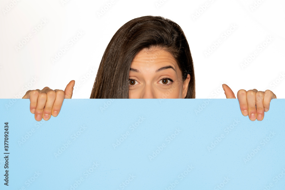 young beautiful woman peeking behind a blue empty board young beautiful woman peeking behind a blue empty board