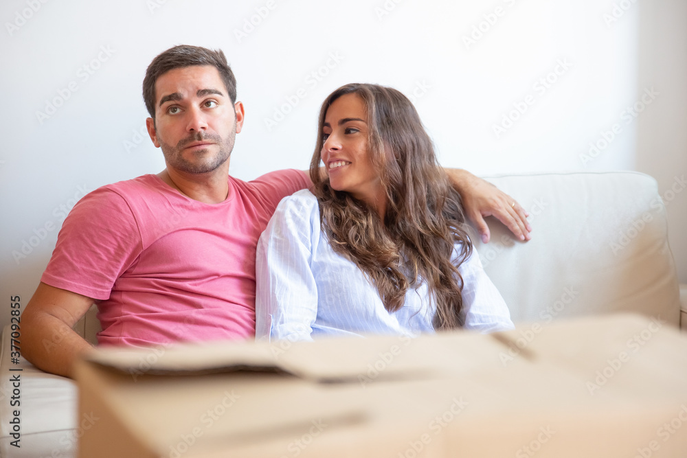 Young Latin couple sitting on couch behind carton box in new apartment, discussing unpacking. Moving or relocation concept Young Latin couple sitting on couch behind carton box in new apartment, discussing unpacking. Moving or relocation concept