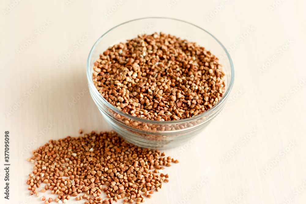 raw buckwheat in a glass cup, buckwheat seeds are scattered nearby raw buckwheat in a glass cup, buckwheat seeds are scattered nearby