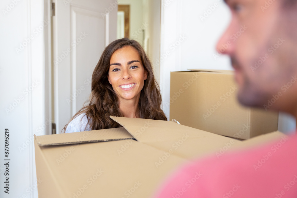 Positive joyful couple moving into new house, carrying carton boxes. Woman looking at camera and smiling. New home concept Positive joyful couple moving into new house, carrying carton boxes. Woman looking at camera and smiling. New home concept