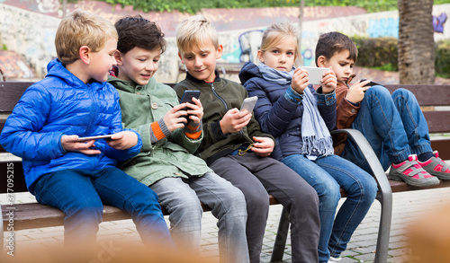 Group of children carried away with phone spending time together outdoors in autumn day