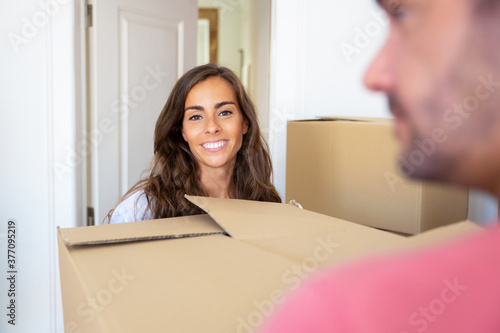 Positive joyful couple moving into new house, carrying carton boxes. Woman looking at camera and smiling. New home concept © Mangostar