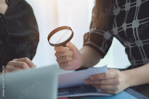 Business woman using magnifying to review balance sheet annual.