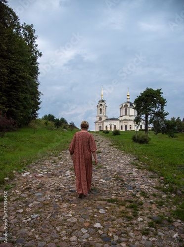 Obraz na plátně An elderly woman walks along a stone-paved path to a temple on a hill