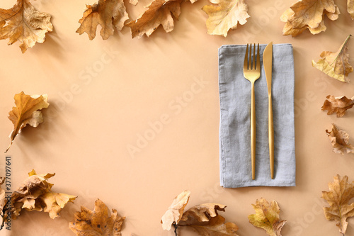 Fall oak leaves as frame and golden cutlery on beige background. Space for design.
