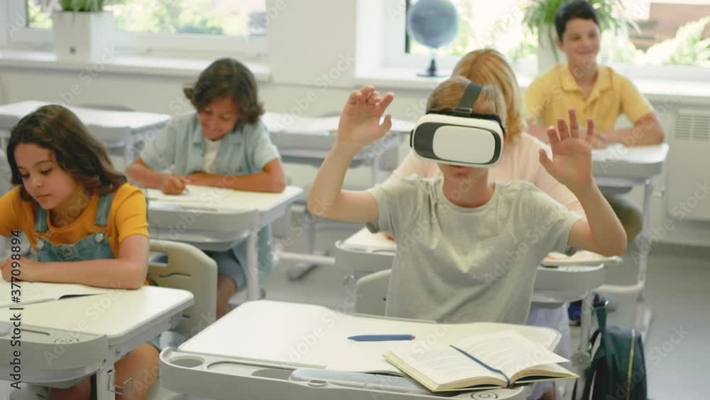 Boy with virtual reality glasses in class. New technologies in the school. Children doing exercises in their notebooks. Boy with virtual reality glasses in class. New technologies in the school. Children doing exercises in their notebooks.