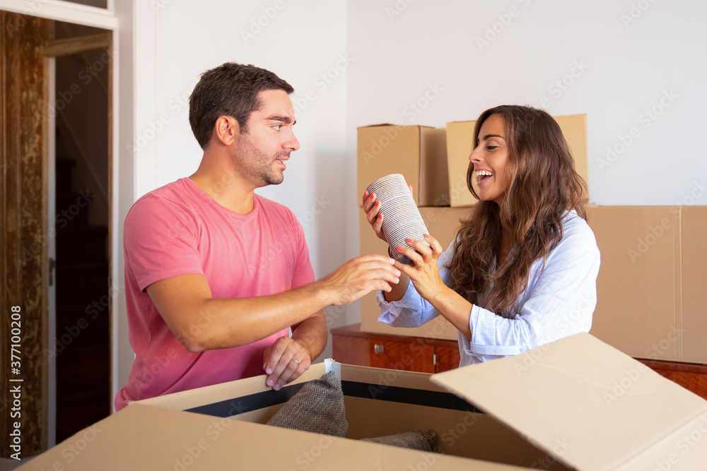 Happy excited young man and woman moving and unpacking things, getting out objects from open carton box. Relocation or new home concept Happy excited young man and woman moving and unpacking things, getting out objects from open carton box. Relocation or new home concept