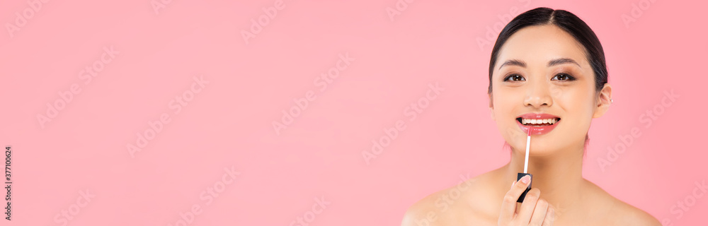 panoramic shot of asian woman applying lip gloss while looking at camera isolated on pink panoramic shot of asian woman applying lip gloss while looking at camera isolated on pink