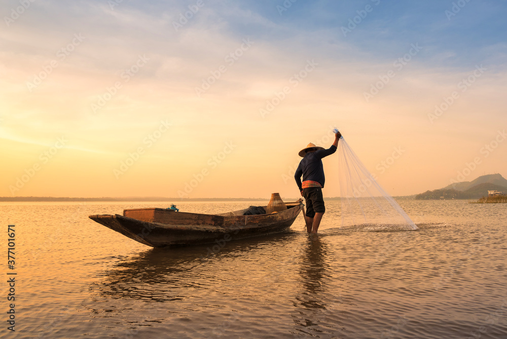 Asian fisherman throwing a net for catching freshwater fish in nature river in the early morning before sunrise
