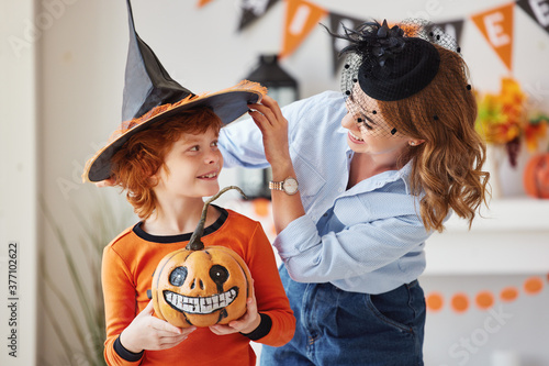 happy family: mother laughs and helps the ginger son to put on a costume for the celebration of Halloween.