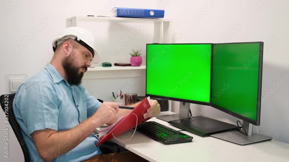 Engineer Wearing Safety Vest and Hardhat Works on a Computer, Two Monitor Screens Show Chroma Key. Green Screen Displays Engineer Wearing Safety Vest and Hardhat Works on a Computer, Two Monitor Screens Show Chroma Key. Green Screen Displays