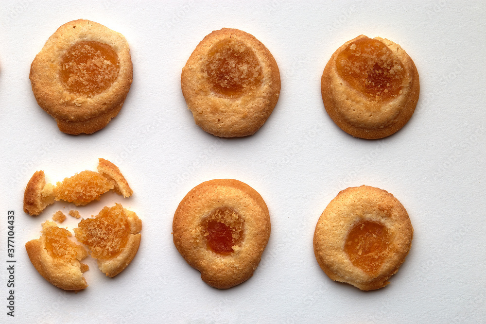 Six handmade cookies with apricot jam arranged in even rows. One in the corner is broken. on white background