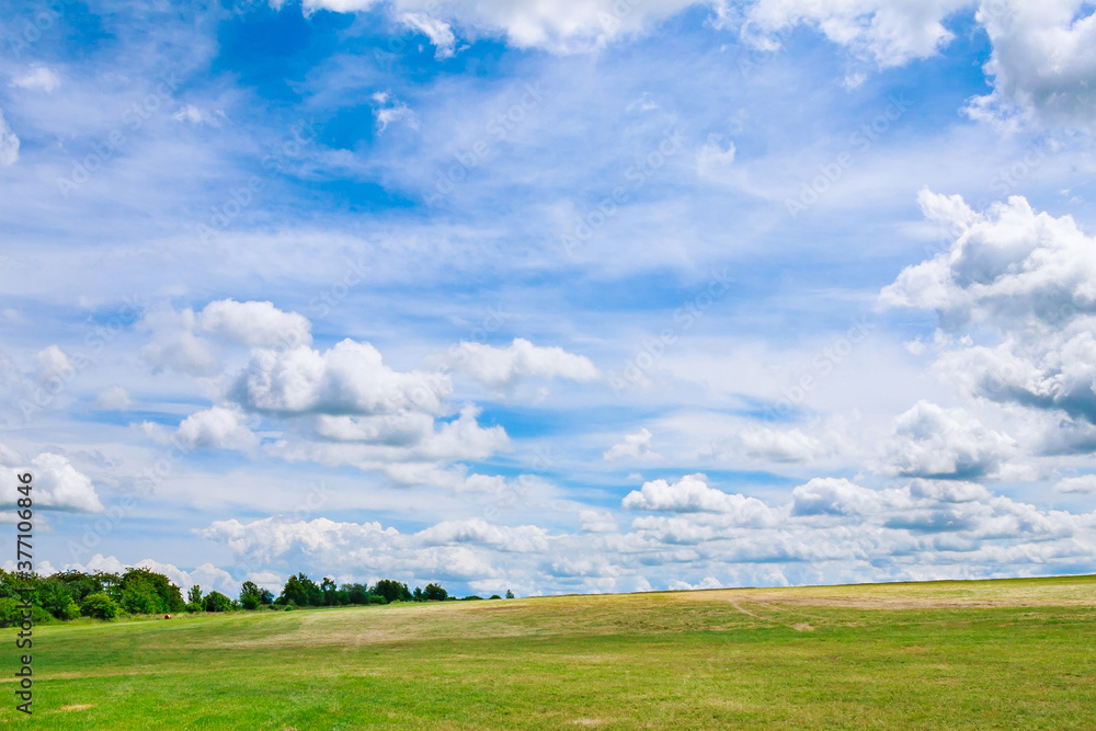 White clouds against a blue sky over a grassy field.