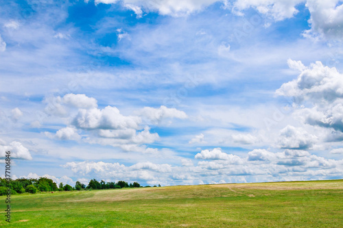 White clouds against a blue sky over a grassy field. © Yaroslav