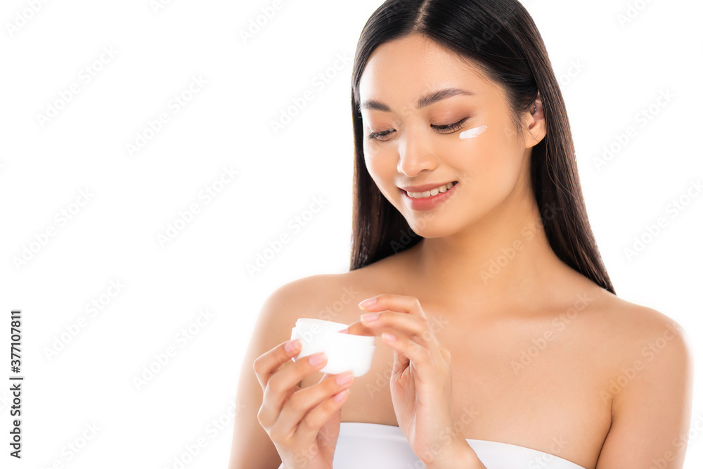 brunette asian woman touching cosmetic cream while applying it on face isolated on white brunette asian woman touching cosmetic cream while applying it on face isolated on white