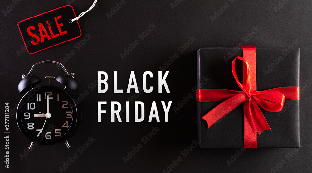 Obraz premium Top view of Black Friday Sale text with black gift box and alarm clock on black background. Shopping concept boxing day and black Friday composition.