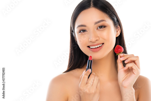 naked asian woman looking at camera while holding sweet strawberry and red lipstick near face isolated on white