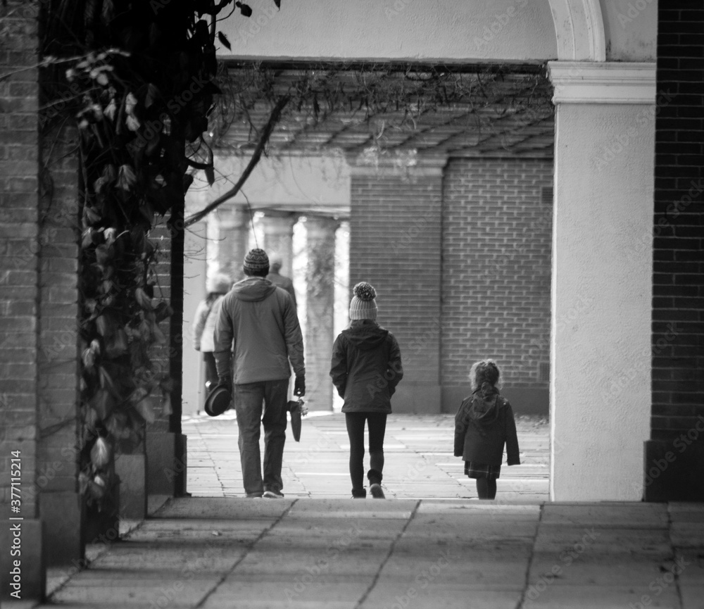 A man and two children walking through an archway, black and white.