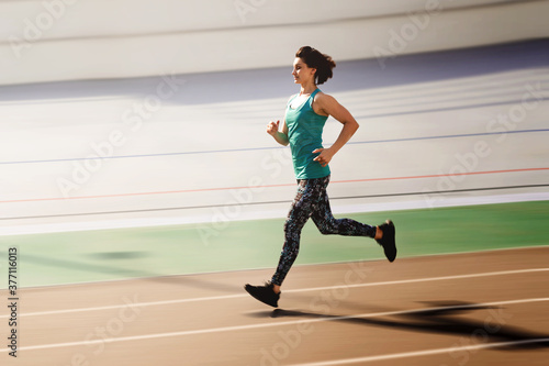 Sporty young woman running by red all-season track at the city stadium.