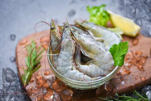 fresh shrimp on bowl and wooden cutting board with rosemary ingredients herb and spices for cooking seafood - raw shrimps prawns on ice frozen at the seafood restaurant