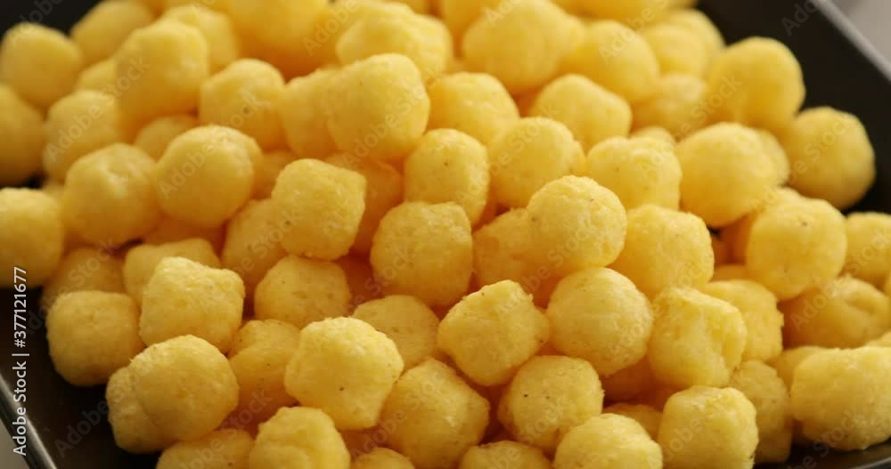 Puffed ball cheese corn chips rotating in black bowl Puffed ball cheese corn chips rotating in black bowl
