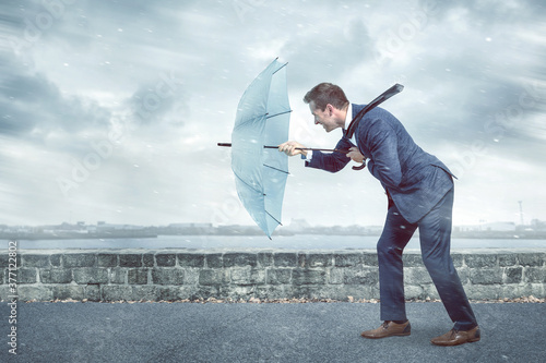 Businessman with an umbrella is facing strong headwind photo
