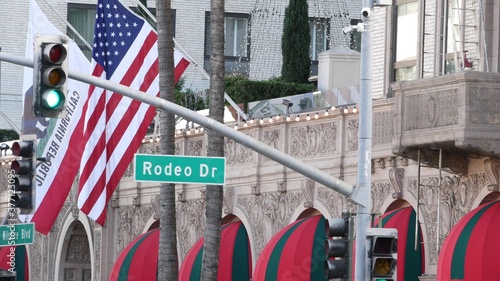 World famous Rodeo Drive Street Road Sign in Beverly Hills against American Unated States flag. Los Angeles, California, USA. Rich wealthy life consumerism, Luxury brands, high-class stores concept.