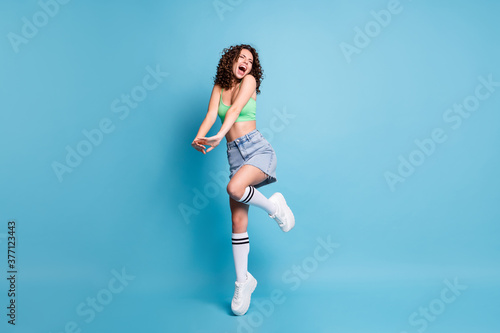 Full body photo of crazy fanatic lady model chilling party concert vacation close eyes raised knee tiptoe slim belly yell sing wear green top jeans skirt isolated pastel blue color background