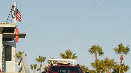 Iconic retro wooden lifeguard watch tower and baywatch red car. Life buoy, american state flag and palm trees against blue sky. Summertime california aesthetic, Santa Monica beach, Los Angeles, CA USA