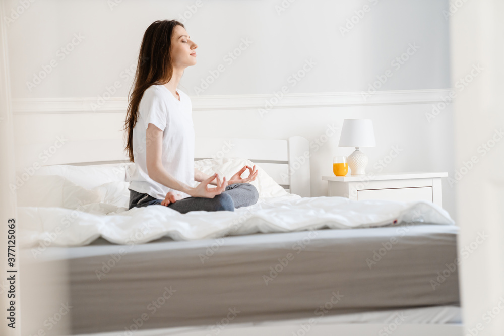 Image of young beautiful girl meditating while sitting in bed Image of young beautiful girl meditating while sitting in bed