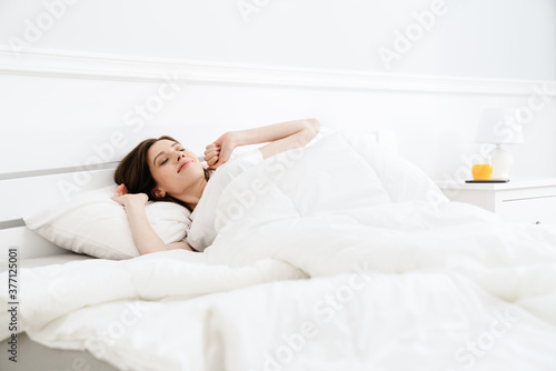 Image of pleased beautiful girl stretching her body while lying in bed