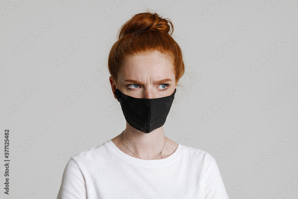 Image of displeased ginger girl in face mask posing and looking aside Image of displeased ginger girl in face mask posing and looking aside