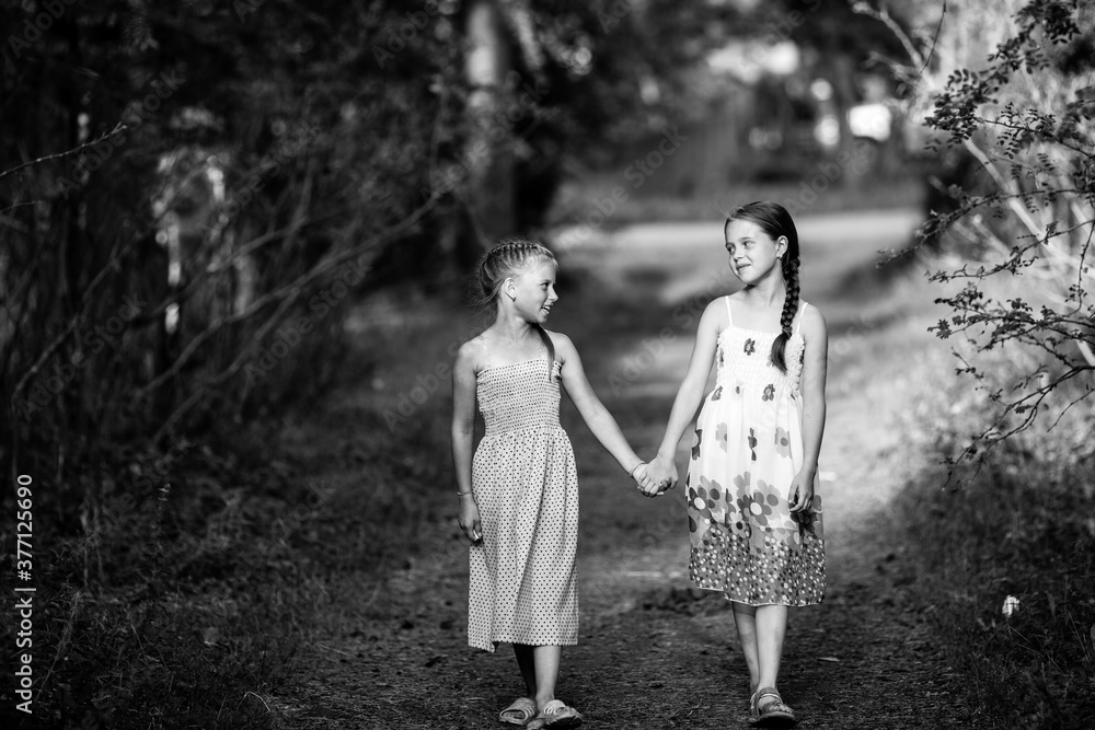 Fototapeta premium Two girlfriends ten-year-old girls walk in the alley. Black and white photo.