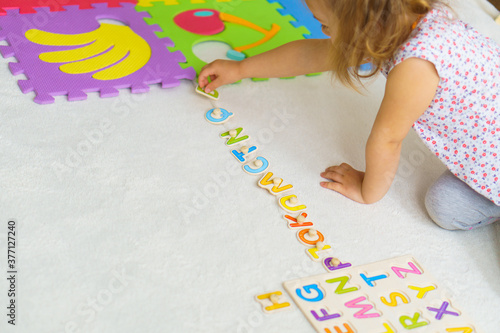 Preparing for school. Education for the youngest. Preschool education in kindergartens. little kid makes puzzles out of alphabet on floor at home.Color English Alphabet for children. puzzles on board